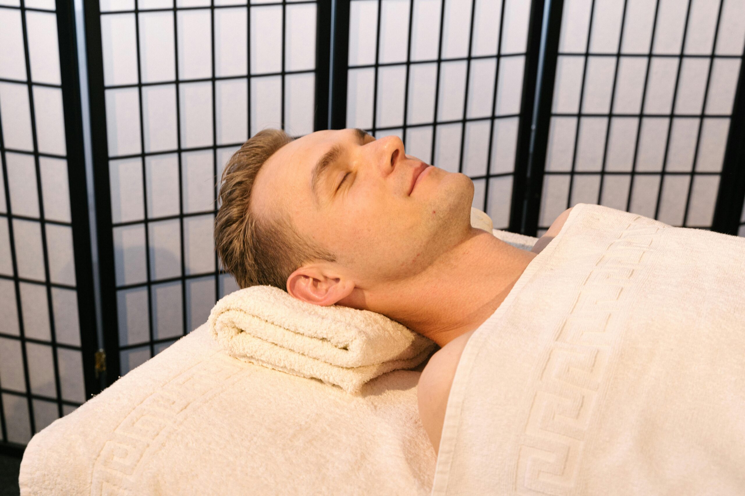 Man reclining at a spa with eyes closed, wrapped in a towel, enjoying relaxation.